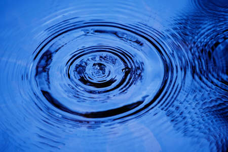Raindrops falling on smooth surface of water. water droplets affect the surface, forming rings on the surface.の写真素材