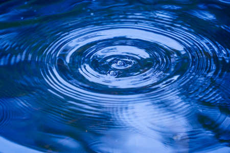 Raindrops falling on smooth surface of water. water droplets affect the surface, forming rings on the surface.の写真素材