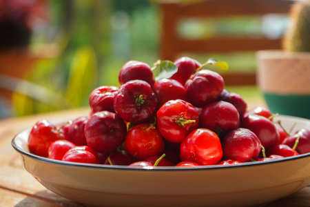 Acerola cherry in white bowl on white wooden background. Fresh organic acerola cherries Thai fruit or acerola cherry on a tree with water droplets, high in vitamin C and antioxidant fruit.の写真素材