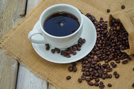 Hot Coffee cup and coffee beans roating on the wooden table beside green garden ranges in the morning sunrise.の写真素材