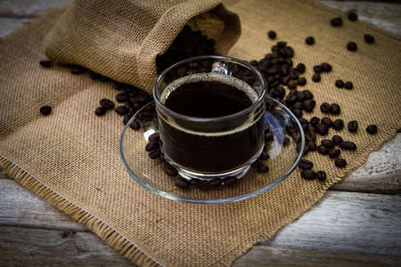 Hot Coffee cup and coffee beans roating on the wooden table beside green garden ranges in the morning sunrise.の写真素材