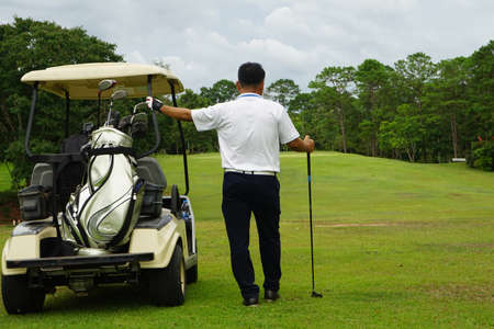 A golfer standing next to a golf cart looks at the golf course to plan the game.の写真素材