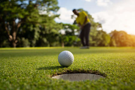 Asian golfer swings in a sand pit during pre-match practice at a golf course. A professional golfer hitting his ball out of a bunker with the sand and ball in mid-air.の写真素材