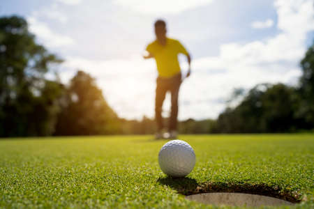 Golfer putting ball on the green golf, lens flare on sun set evening time. Blurred golfer playing golf in beautiful golf course in the evening golf course with sunshine.の写真素材