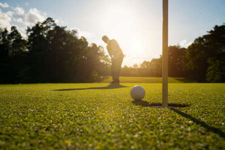 Golfer putting ball on the green golf, lens flare on sun set evening time. Blurred golfer playing golf in beautiful golf course in the evening golf course with sunshine.の写真素材