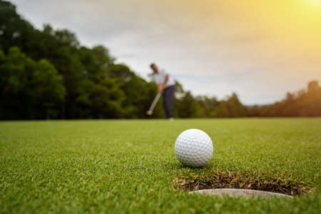 Golfer putting ball on the green golf, lens flare on sun set evening time. Blurred golfer playing golf in beautiful golf course in the evening golf course with sunshine.の写真素材