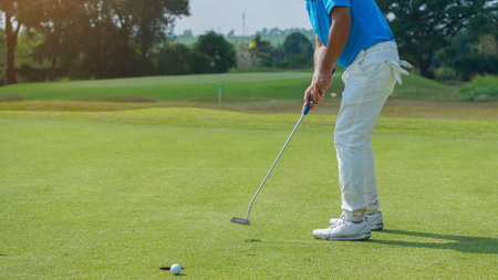 Golfer putting ball on the green golf, lens flare on sun set evening time. Golfer action to win after long putting golf ball in to the hole.の写真素材