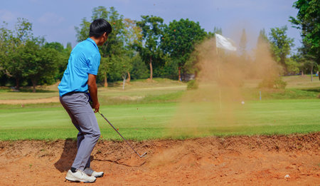golfer hits a ball off a sand bunker, the hurdles of the golf course. Golfer playing golf in the evening golf course, on sun set evening timeの写真素材
