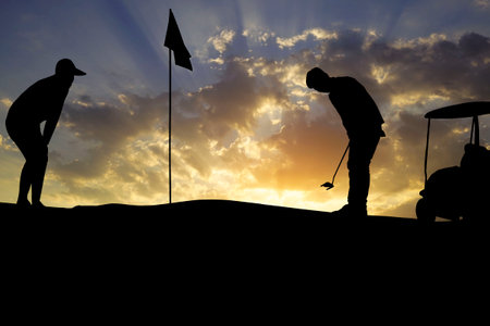Golfers' hit golf ball toward the hole at sunset silhouetted. Golden morning sky in winter, misty high mountain background.の写真素材