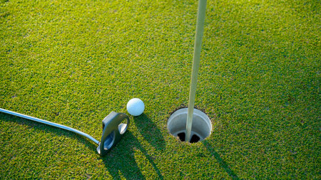 Selective focus. white golf ball in hole on green grass good for background with sunlight. Putter and golf ball beside the golf hole.の写真素材