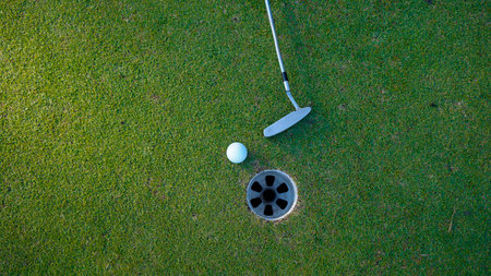 Selective focus. white golf ball in hole on green grass good for background with sunlight. Putter...