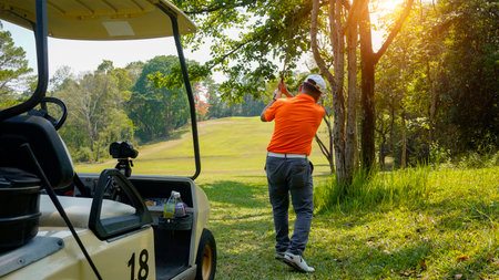 Golfer plays golf on the fairway with golf cart in the evening at sunset background. Sport holiday lifestyle concept.の写真素材