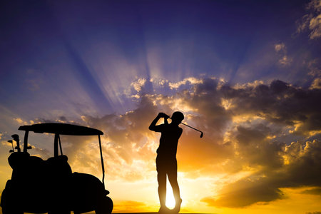 Golfers' hit golf ball toward the hole at sunset silhouetted. Golden morning sky in winter, misty high mountain background.の写真素材