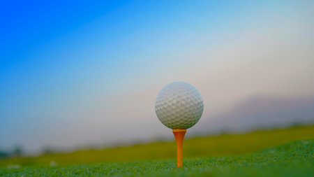 Golf ball on green grass in the evening golf course with sunshine background. Close-up golf ball on tee with blur green bokeh background.の写真素材