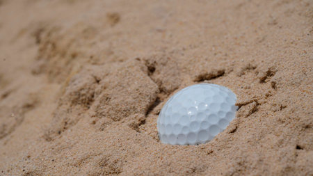 Golf ball in bunker sand. Golf ball on the sand in beautiful golf course at sunset background.の写真素材