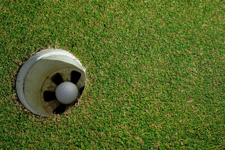 Selective focus. white golf ball in hole on green grass ackground with sunlight.の写真素材