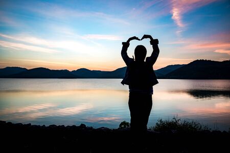 Silhouette of Women hand-made heart-shaped the lagoon looking at sunrise.