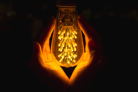 Light bulb with hand, Hand under light bulb, vintage light bulbs in dark time of the day, warming up handsの写真素材
