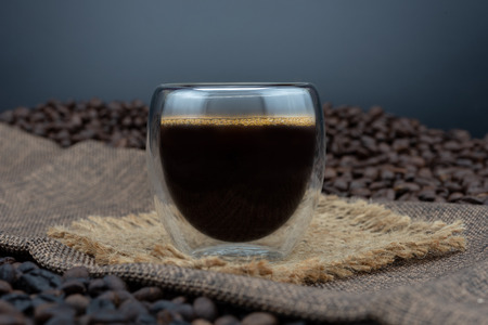 Coffee cup and coffee beans on black background. black coffee in a double-bottomed glass.の写真素材
