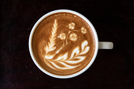 Close up white coffee cup with heart shape latte art foam on black wood table near window. Top view latte art coffee cup.の写真素材
