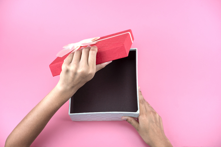 hands hold a empty red and white gift box on pink background for holiday, christmas, thanks giving day, birthday. Young woman hands holding red gift box.の写真素材
