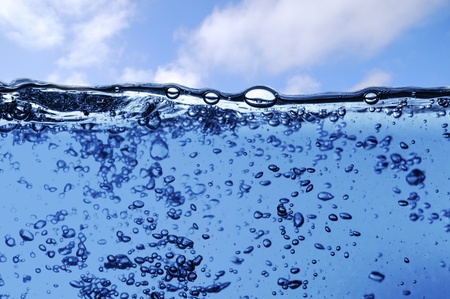 Air bubbles in ocean water rise to the surface with cloudy sky with sun in the backgroundの写真素材