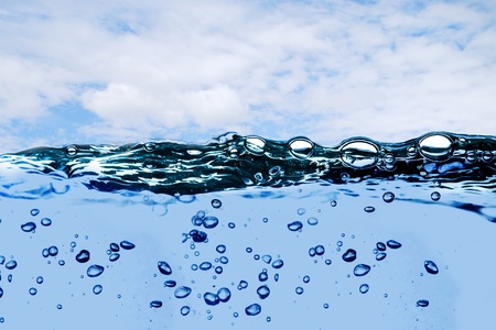 Air bubbles in ocean water rise to the surface with cloudy sky with sun in the backgroundの写真素材