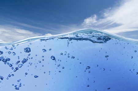 Air bubbles in ocean water rise to the surface with cloudy sky with sun in the background