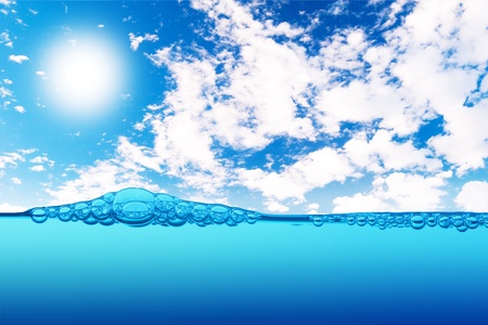 Air bubbles in ocean water rise to the surface with cloudy sky with sun in the backgroundの写真素材