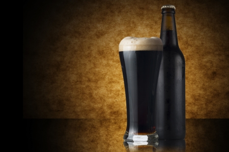 Glass of dark beer and bottle on yellow backgroundの写真素材