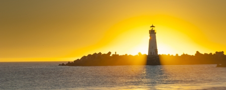 Lighthouse with sunset in the background and ocean in the foregroundの写真素材