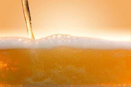 Beer pouring into a glass on a yellow background. Close-up