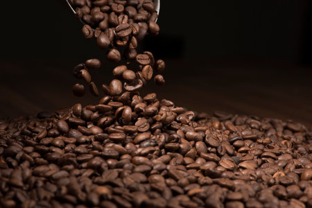 Coffee beans being poured from a coffee grinder on a wooden tableの写真素材