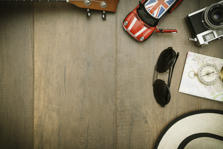 Travel accessories costumes. Passports, luggage, hat,guitar, travel maps,camera prepared for the trip place on brown wood texture,retro tone with vignetteの写真素材