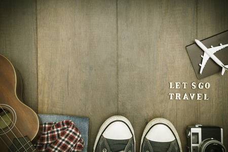 Travel accessories costumes. Passports, luggage, hat,guitar, travel maps,camera prepared for the trip place on brown wood texture,retro tone with vignetteの写真素材