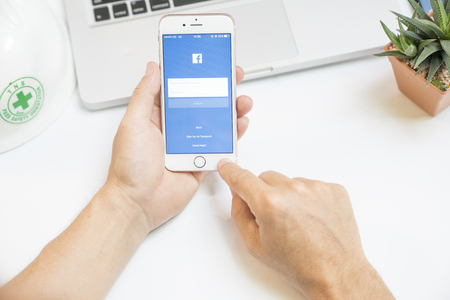 Bangkok,Thailand March 4 2017 : Notebook and safety helmet and hand holding iPhone 6 with social network service Facebook on the screen. iPhone was created and developed by the Apple inc.のeditorial素材