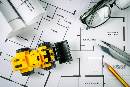 Top view of architect drawing on non identified architectural project with various of tools such as divider pencil eye glassed and small heavy equipment machine toysの写真素材