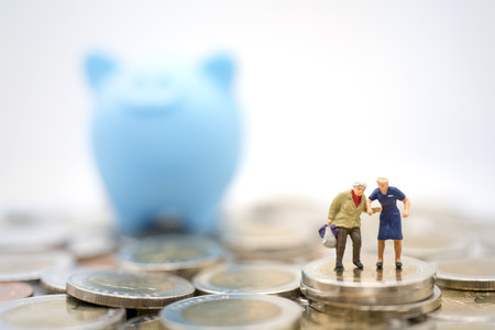 Miniature toy:Old man shopping or travel after retired on stack of coins and piggy bank. Saving money for after retire,business,shopping,travel conceptの写真素材