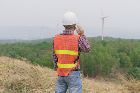 Success engineer man talking mobile during working with wind turbine on the high hill mountain.On hand holding tablet .Wind turbine electric generator,clean energy concept.の写真素材