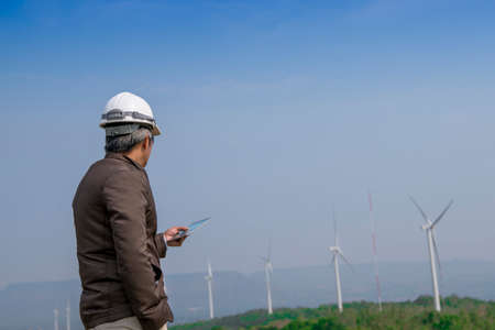 Senior engineer man with safety helmet looking to wind turbine for checking its working on the high...