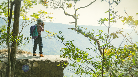 Relaxed backpacker traveler take photo with camera at the edge of mountain,feel free and happy.Concept of vacation,freedom,happiness,enjoyment ,summer and well being.の写真素材