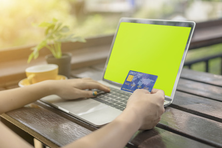 Young woman holding plastic credit card and using laptop computer for shopping online at coffee...