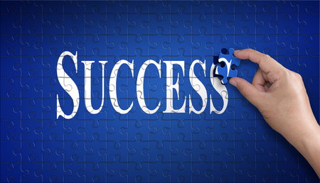 Success word on Jigsaw puzzle ? business concept. Man hand holding a blue puzzle to complete the word Success divided over them concept of the solution to a problem, challenge, plan and strategy.の写真素材