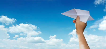Taking flight. Man's hand holding paper plane in sky show concept of journey, travel, dream, freedom, start up, new business. Hand is throwing paper airplane against blue sky with empty space for textの写真素材
