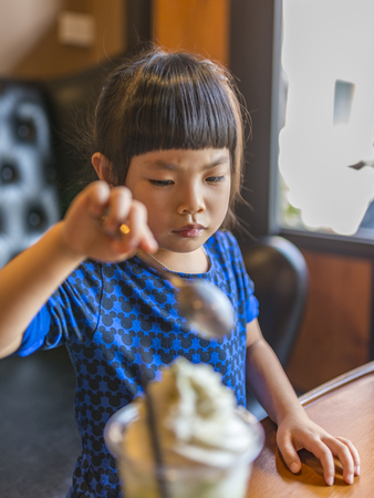 Asian little girl use spoon for cream in softdrinkの写真素材