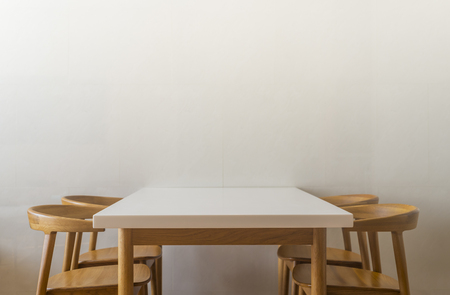 White table in white room and empty space over the table. Nothing on table. Wooden chairs.