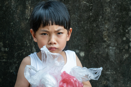 Asian little girl is holding plastic bags with her arms. Serious face about problem of plastic bag for her generation.の写真素材