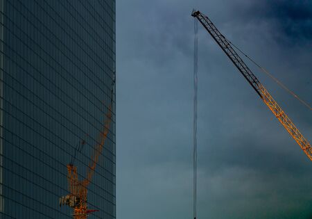 Crane and reflection on mirror building, dark sky before storm.