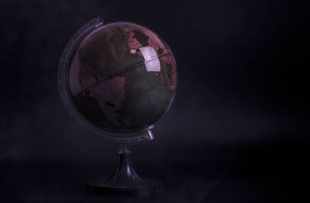 Globe model on stand holder in dark mood tone, adjusted toning, black background. Concept for crucial time, hard time, weakness of global earth. Purple light ambient with soft smoke.の写真素材