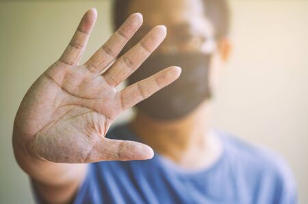 Blurred Asian man showing gesture STOP. Healthy man wears medical protective black mask against...